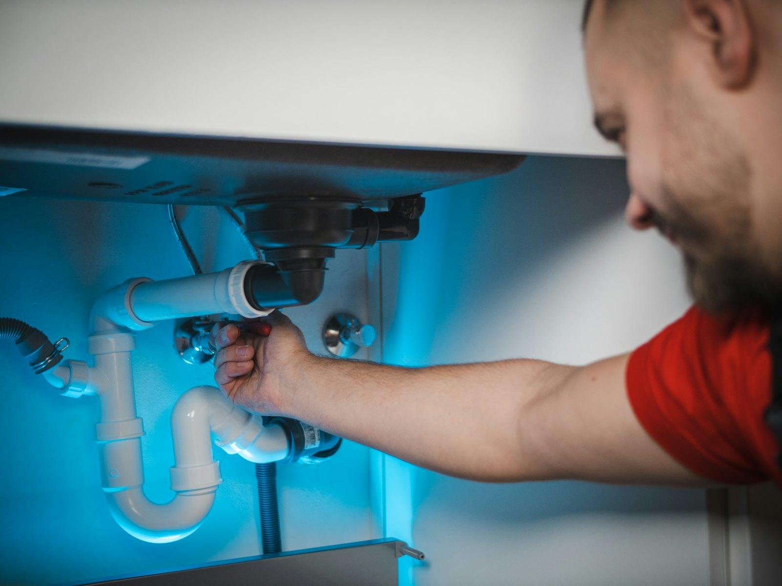 Plombier réparant un siphon sous un évier, éclairage bleu